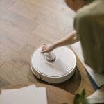 A woman interacts with a robotic vacuum on a wooden floor, showcasing smart home technology.