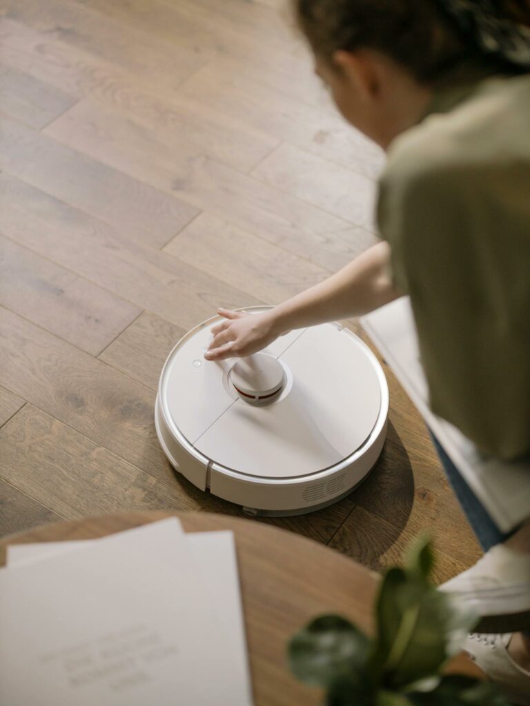 A woman interacts with a robotic vacuum on a wooden floor, showcasing smart home technology.