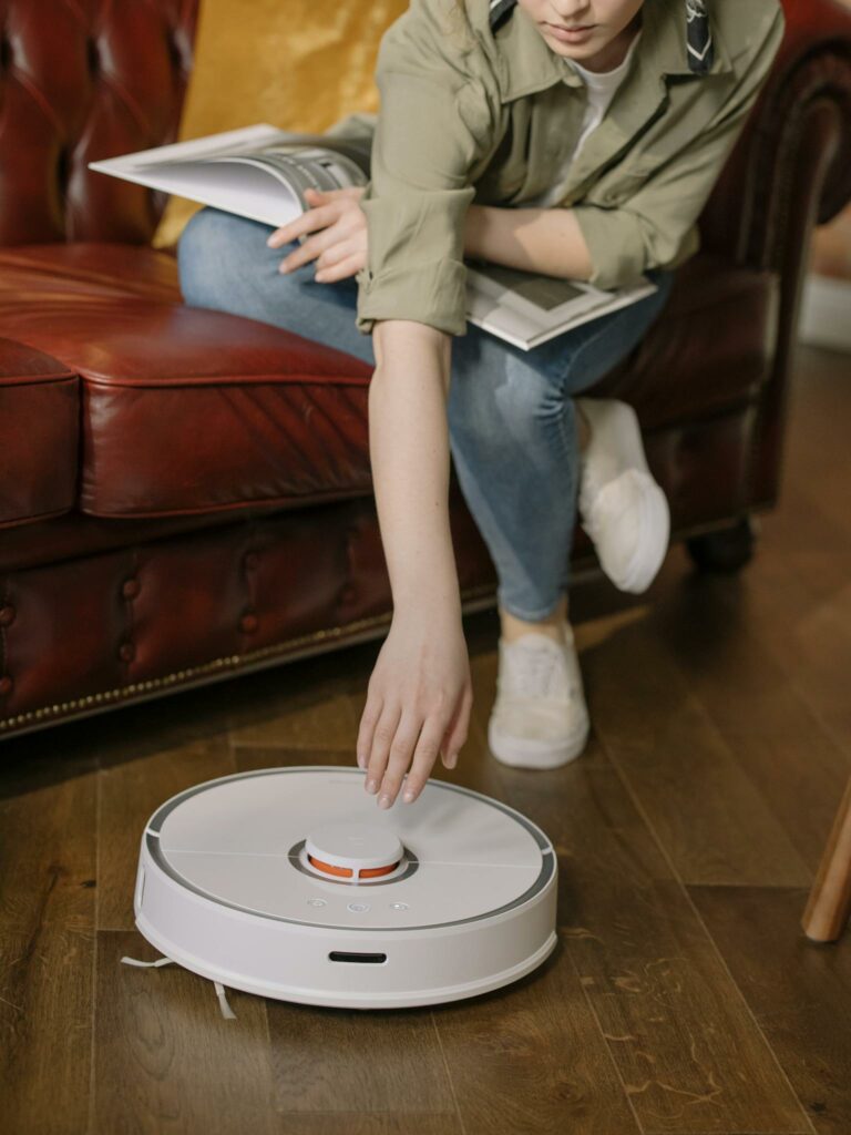Person relaxing in cozy living room while operating a robot vacuum cleaner on wooden floor.